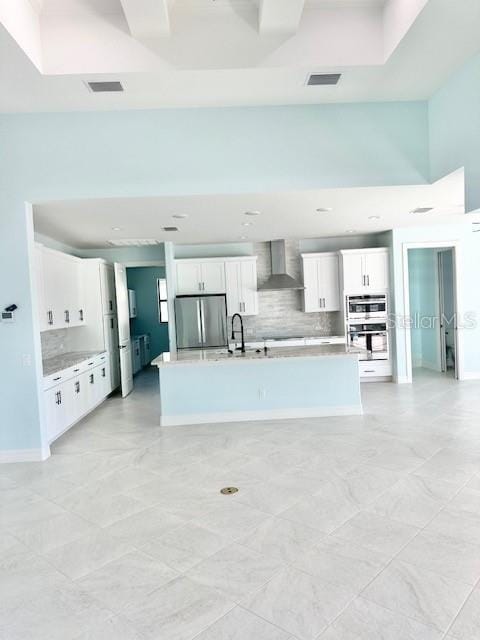 kitchen with light countertops, visible vents, appliances with stainless steel finishes, white cabinets, and wall chimney range hood