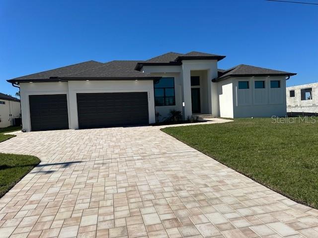 prairie-style home with a garage, a front yard, decorative driveway, and stucco siding