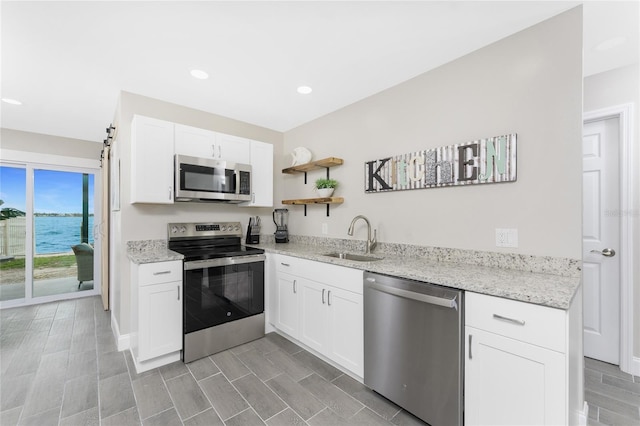 kitchen featuring light stone countertops, stainless steel appliances, white cabinetry, open shelves, and a sink