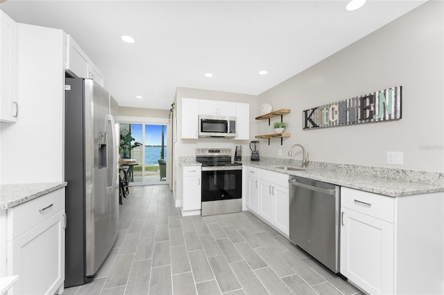 kitchen featuring open shelves, white cabinetry, stainless steel appliances, and a sink