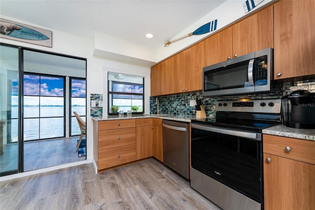 kitchen featuring light stone counters, brown cabinets, light wood finished floors, backsplash, and appliances with stainless steel finishes