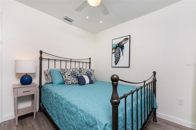 bedroom with a ceiling fan, visible vents, baseboards, and wood finished floors