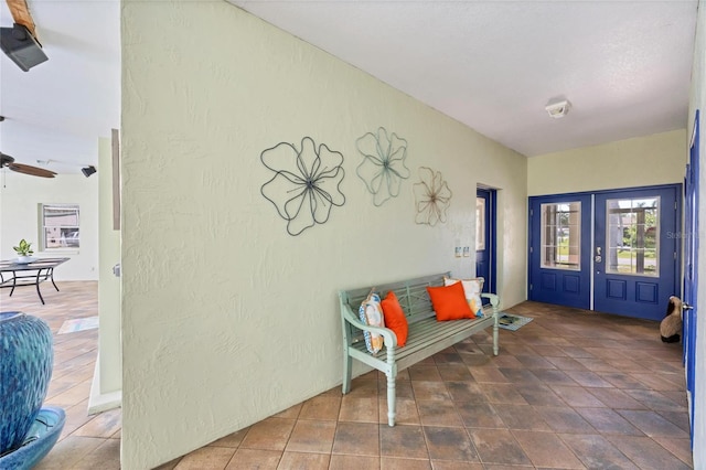 interior space featuring a textured wall, a ceiling fan, and french doors