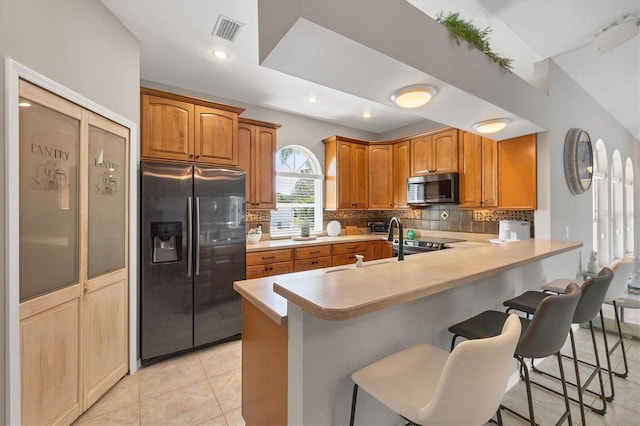 kitchen featuring a breakfast bar area, stainless steel appliances, visible vents, light countertops, and backsplash