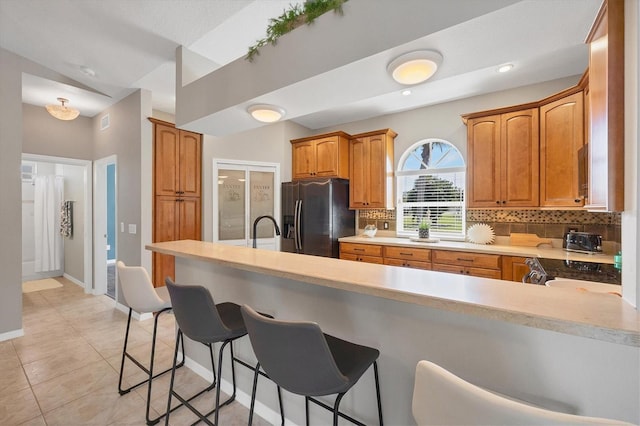 kitchen with a peninsula, a kitchen breakfast bar, light countertops, tasteful backsplash, and stainless steel fridge