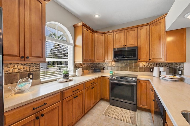 kitchen with tasteful backsplash, brown cabinets, stainless steel appliances, light countertops, and light tile patterned flooring