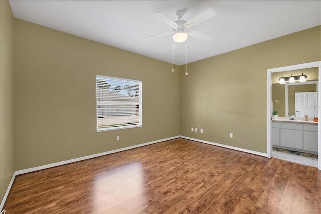 unfurnished bedroom featuring ceiling fan, a sink, connected bathroom, wood finished floors, and baseboards