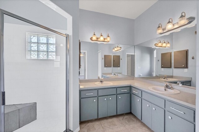 bathroom featuring tile patterned flooring, tiled shower, a sink, and double vanity