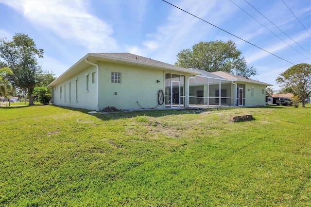 rear view of house with glass enclosure, a lawn, and stucco siding