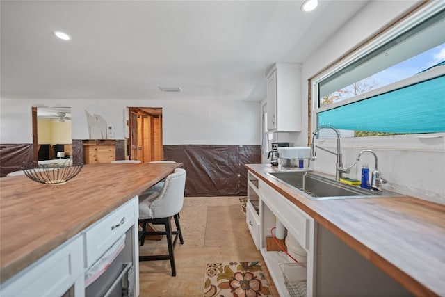 kitchen featuring wooden counters, visible vents, white cabinets, and a sink