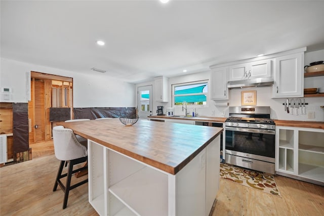 kitchen with butcher block countertops, stainless steel range with gas cooktop, white cabinetry, open shelves, and a sink