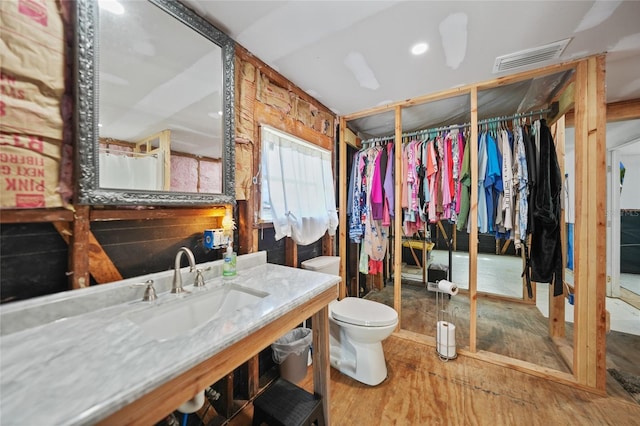 bathroom with toilet, wood finished floors, a sink, visible vents, and a walk in closet