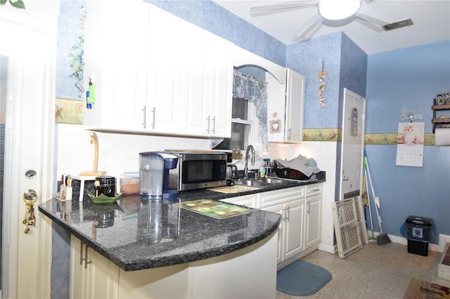 kitchen featuring a peninsula, a sink, white cabinetry, dark stone counters, and stainless steel microwave