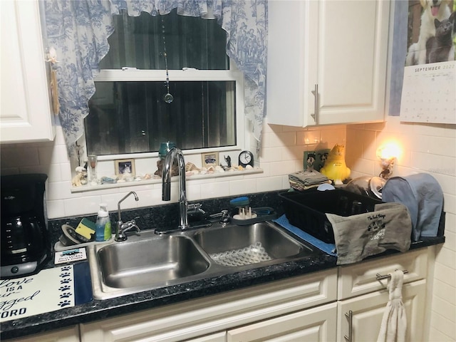 kitchen featuring dark countertops, backsplash, white cabinets, and a sink