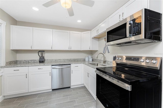 kitchen featuring white cabinets, light stone counters, appliances with stainless steel finishes, a sink, and recessed lighting