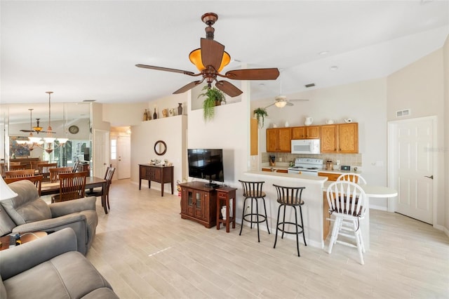 living room with light wood-type flooring, visible vents, high vaulted ceiling, and a ceiling fan