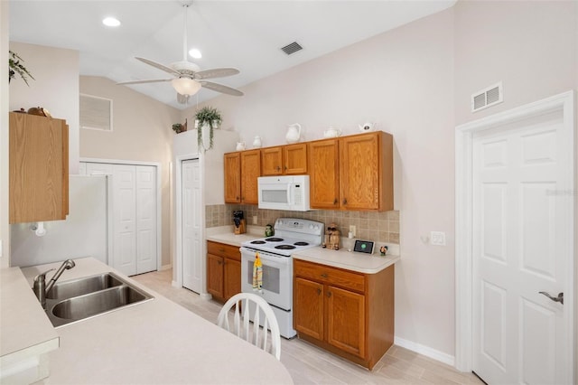 kitchen featuring visible vents, a sink, white appliances, brown cabinetry, and vaulted ceiling