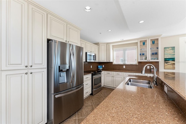 kitchen with recessed lighting, stainless steel appliances, a sink, backsplash, and glass insert cabinets