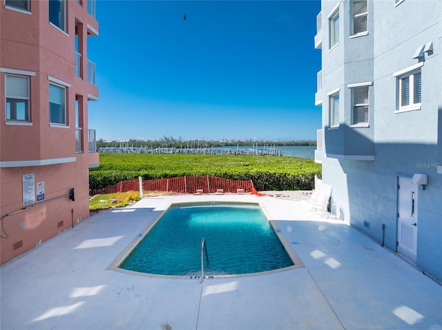 pool featuring a water view, a patio area, and fence