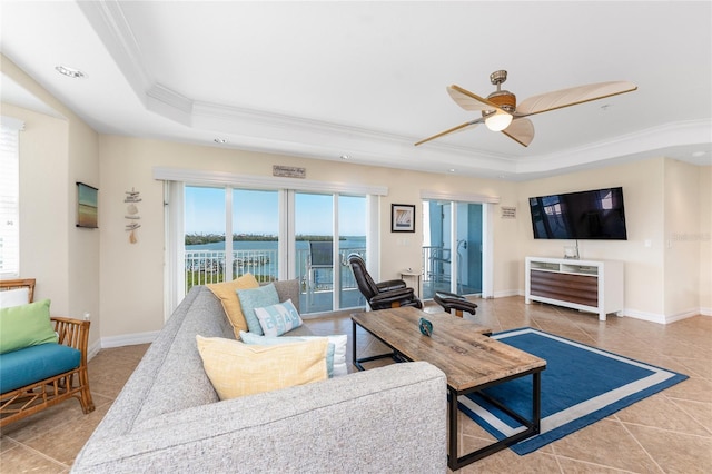 tiled living room featuring a tray ceiling, crown molding, baseboards, and ceiling fan