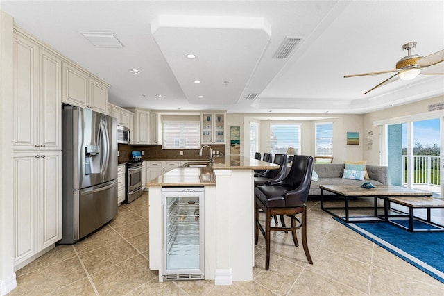 kitchen featuring beverage cooler, stainless steel appliances, visible vents, a kitchen breakfast bar, and plenty of natural light