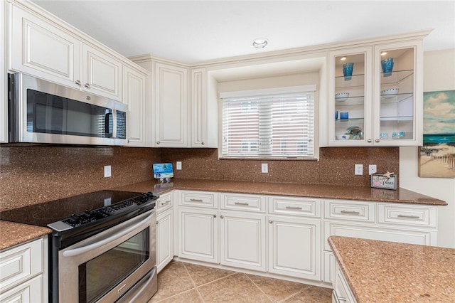 kitchen featuring tasteful backsplash, glass insert cabinets, dark stone countertops, stainless steel appliances, and light tile patterned flooring