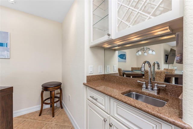 kitchen with dark stone counters, glass insert cabinets, white cabinetry, a sink, and light tile patterned flooring