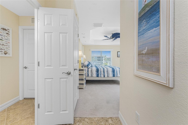 carpeted bedroom with a tray ceiling, a ceiling fan, visible vents, and baseboards