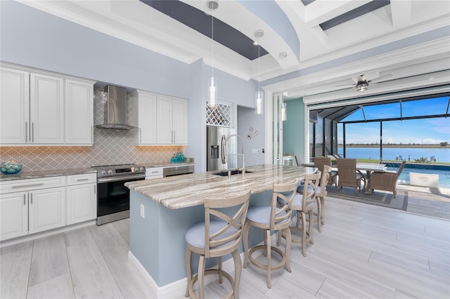 kitchen featuring a water view, wall chimney range hood, appliances with stainless steel finishes, and white cabinets