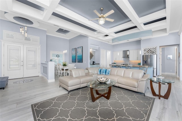 living room with a towering ceiling, light wood finished floors, and coffered ceiling