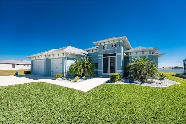 view of front of home with stucco siding, concrete driveway, a water view, an attached garage, and a front lawn