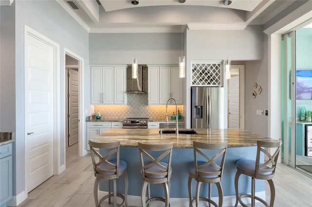 kitchen featuring tasteful backsplash, white cabinets, wall chimney exhaust hood, appliances with stainless steel finishes, and a sink