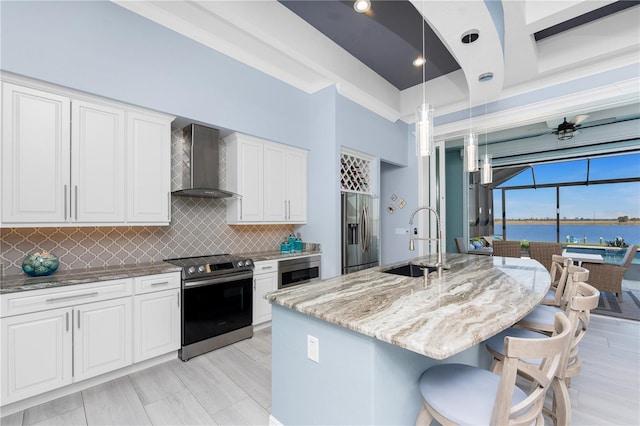 kitchen featuring light stone countertops, a sink, wall chimney range hood, appliances with stainless steel finishes, and decorative backsplash