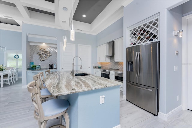 kitchen featuring a breakfast bar, stainless steel appliances, white cabinetry, a sink, and wall chimney range hood