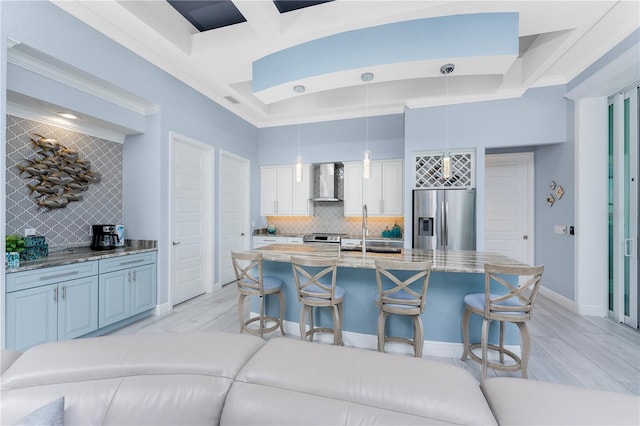 kitchen featuring white cabinetry, appliances with stainless steel finishes, wall chimney range hood, backsplash, and a kitchen bar