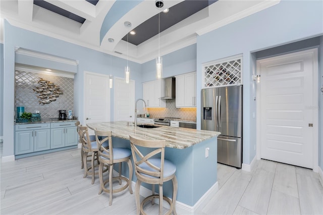 kitchen with a sink, appliances with stainless steel finishes, light stone countertops, wall chimney exhaust hood, and an island with sink