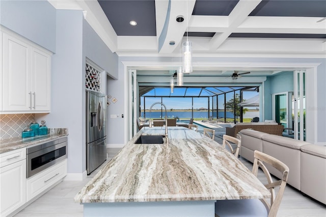 kitchen with stainless steel appliances, a water view, a sink, a sunroom, and backsplash