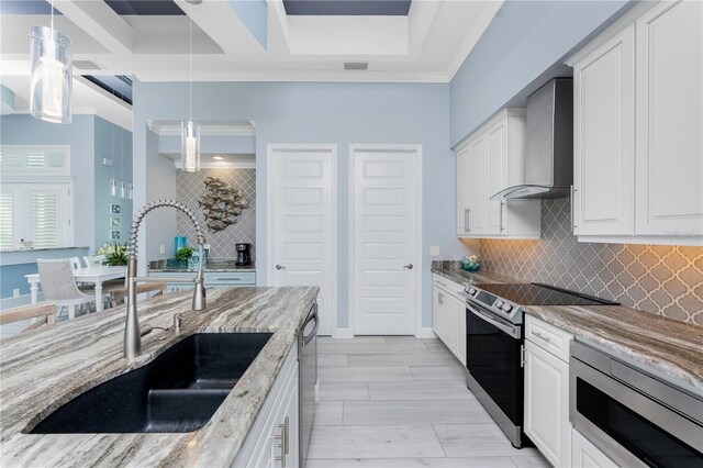 kitchen featuring wall chimney exhaust hood, light stone countertops, stainless steel appliances, white cabinetry, and a sink