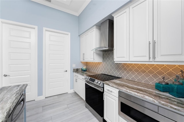 kitchen with wall chimney range hood, tasteful backsplash, appliances with stainless steel finishes, and white cabinets