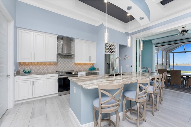 kitchen featuring light stone counters, stainless steel appliances, a sink, white cabinetry, and wall chimney range hood