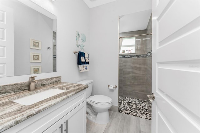 full bathroom featuring a tile shower, vanity, and toilet