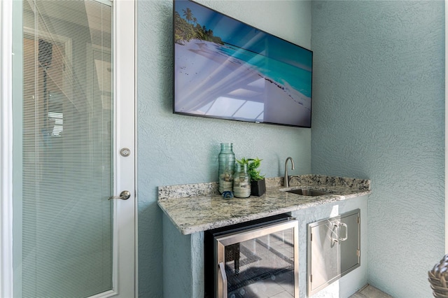 bar with beverage cooler, a textured wall, a sink, and wet bar