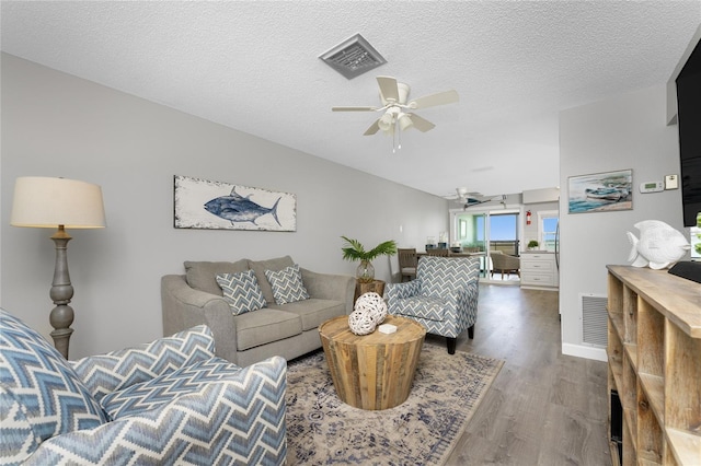 living area featuring a textured ceiling, wood finished floors, visible vents, and a ceiling fan