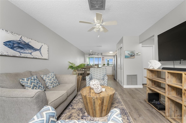 living area featuring ceiling fan, a textured ceiling, visible vents, and wood finished floors