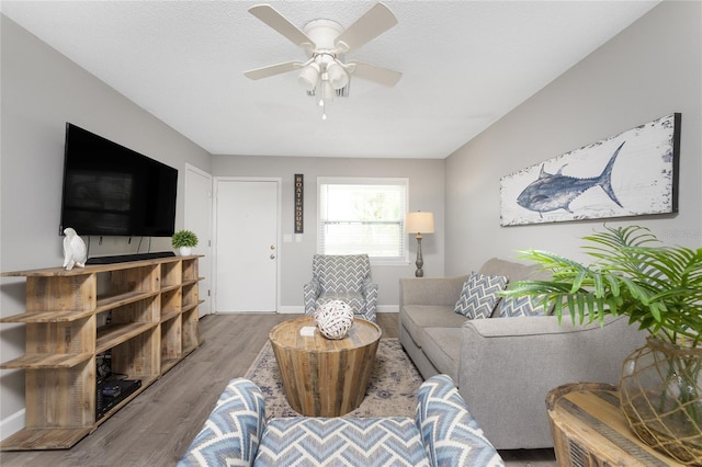 living area featuring ceiling fan, a textured ceiling, baseboards, and wood finished floors