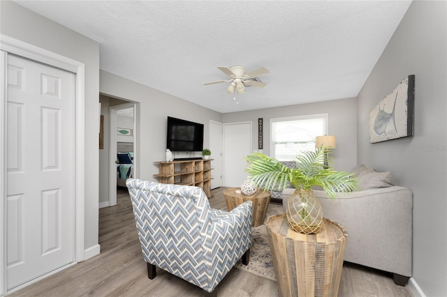 living area with light wood-style floors, a textured ceiling, and a ceiling fan