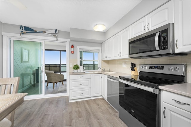 kitchen featuring stainless steel appliances, white cabinets, light countertops, backsplash, and light wood finished floors