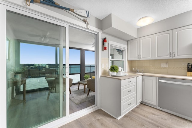 kitchen featuring light wood-style flooring, white cabinets, light countertops, backsplash, and dishwasher