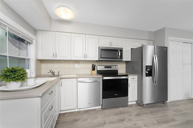 kitchen featuring light countertops, decorative backsplash, appliances with stainless steel finishes, white cabinets, and light wood-type flooring