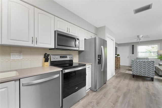 kitchen with stainless steel appliances, visible vents, white cabinets, light wood-type flooring, and tasteful backsplash